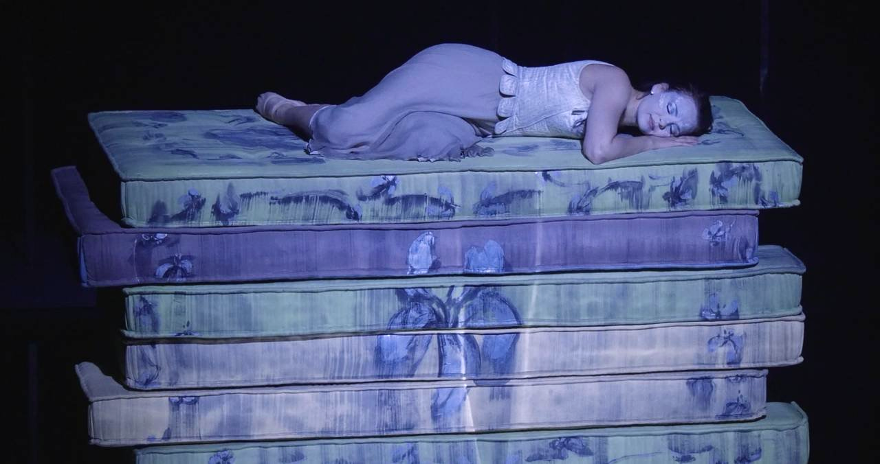Girl sleeping on a pile of matresses reminiscent of the fairy tale " The Princess and the pea"