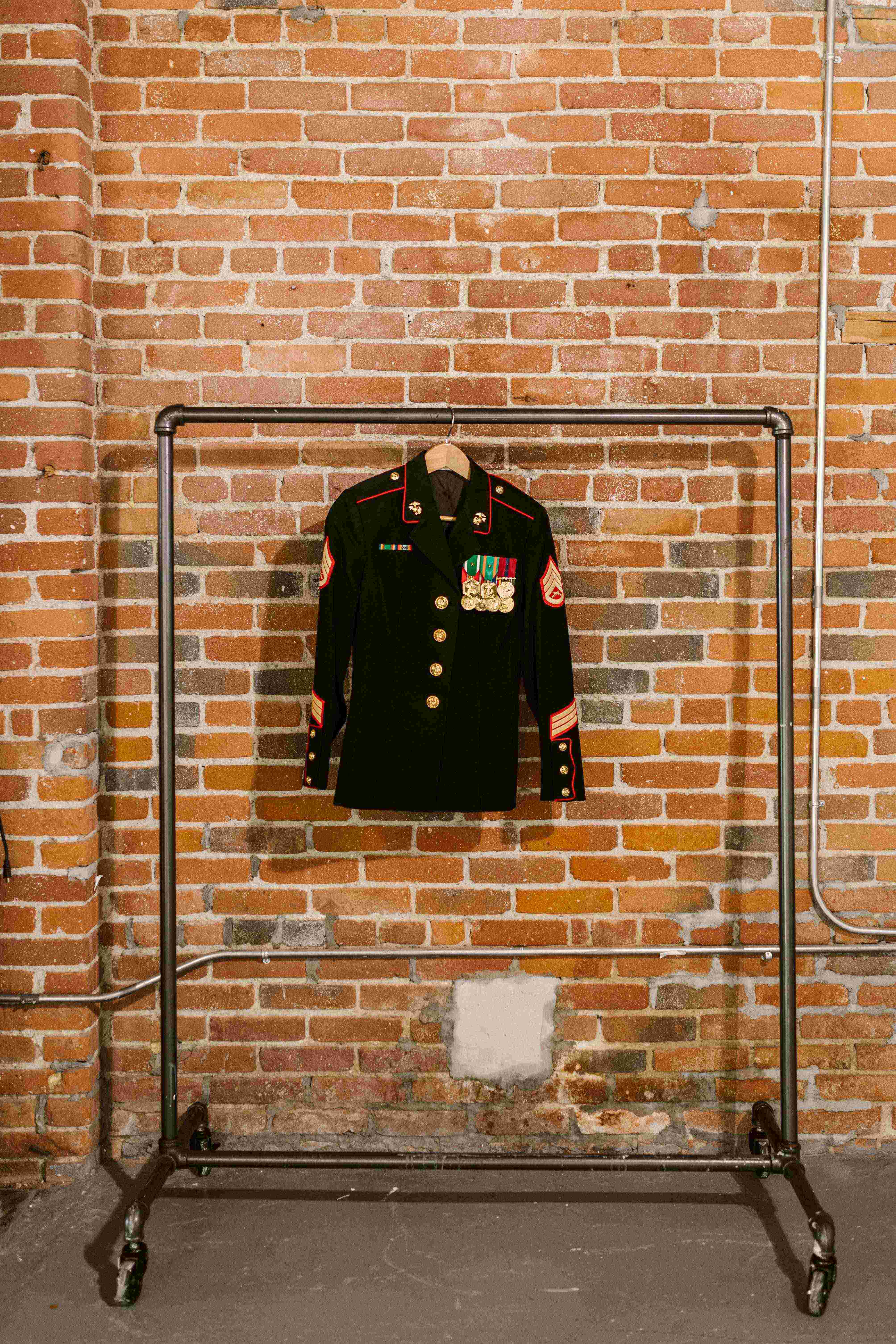 Coat rack from water pipe against background of brick wall with black dress jacket from military uniform hanging